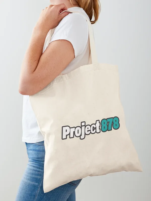 Person carrying a natural canvas tote bag with the Project 878 logo